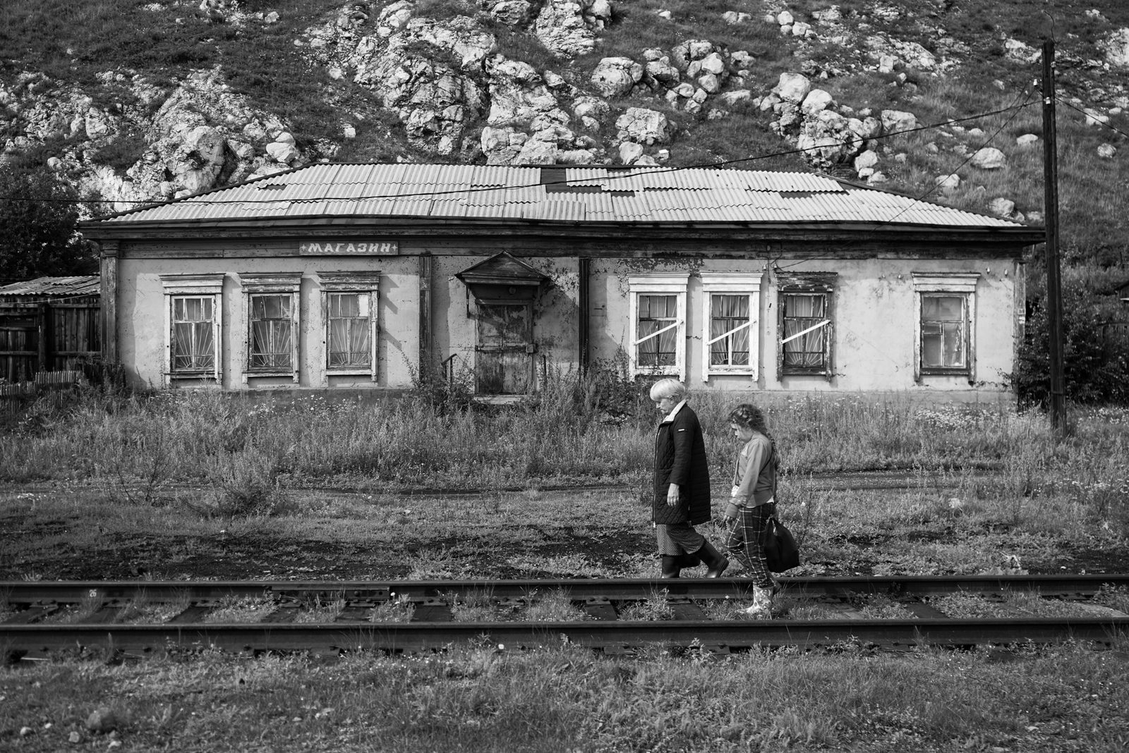 Black-and-white view of a low wooden house, two small figures standing in front — Lake Baikal