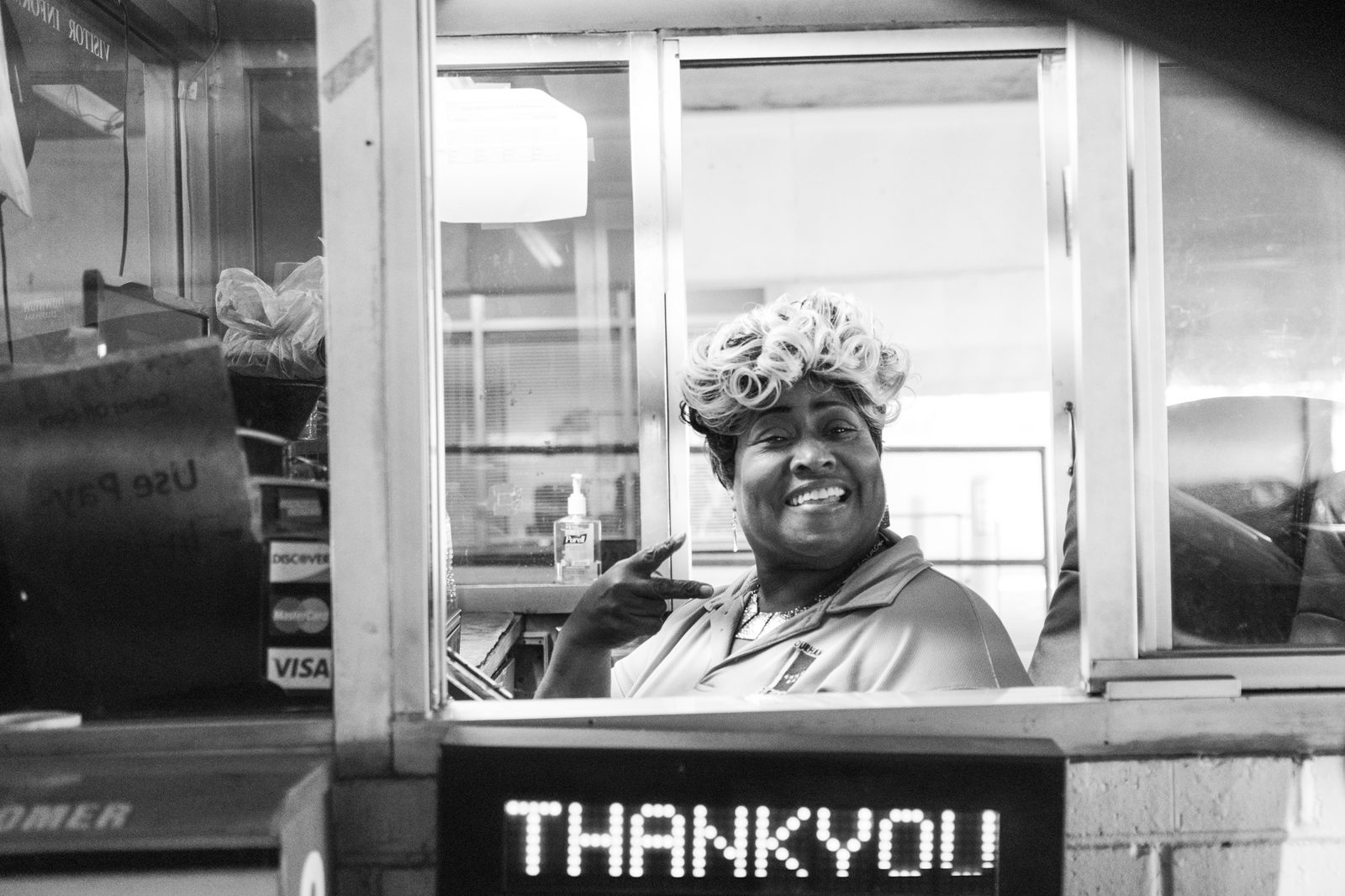 Black-and-white portrait of a smiling woman at a service window above a lit Thank You sign — Chapel Hill
