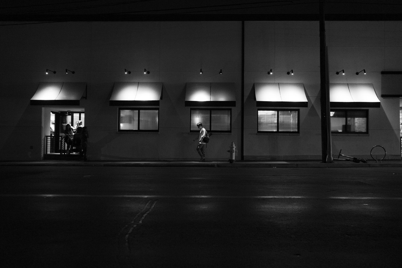 Black-and-white view of a building facade at night, windows lit beneath awnings — Miami