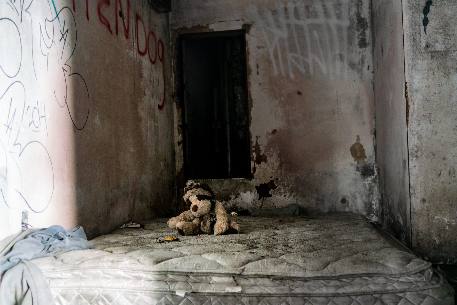 A worn teddy bear on a bare mattress in a derelict, graffiti-marked room — Detroit