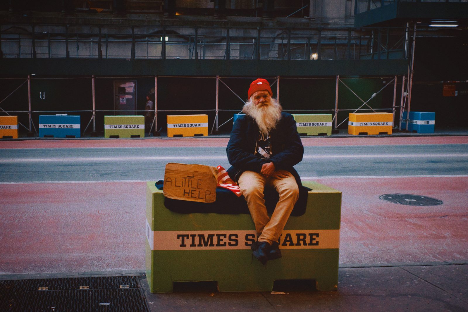A woman seated alone on a bench in a lit plaza at night — New York