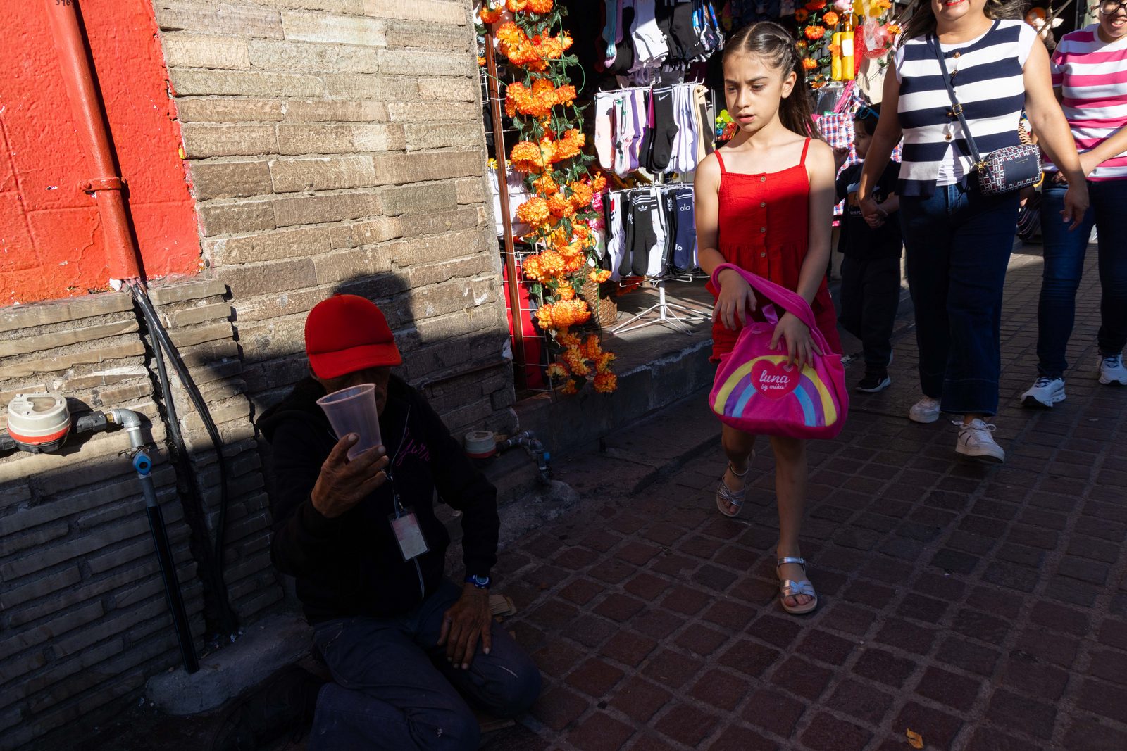 A girl in a red dress walks through a busy market street — The Liminal Innocence