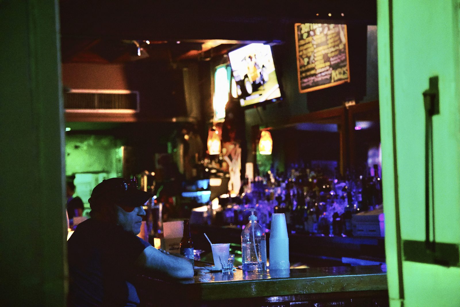 Inside a bar washed in green light, patrons at the counter — New Orleans