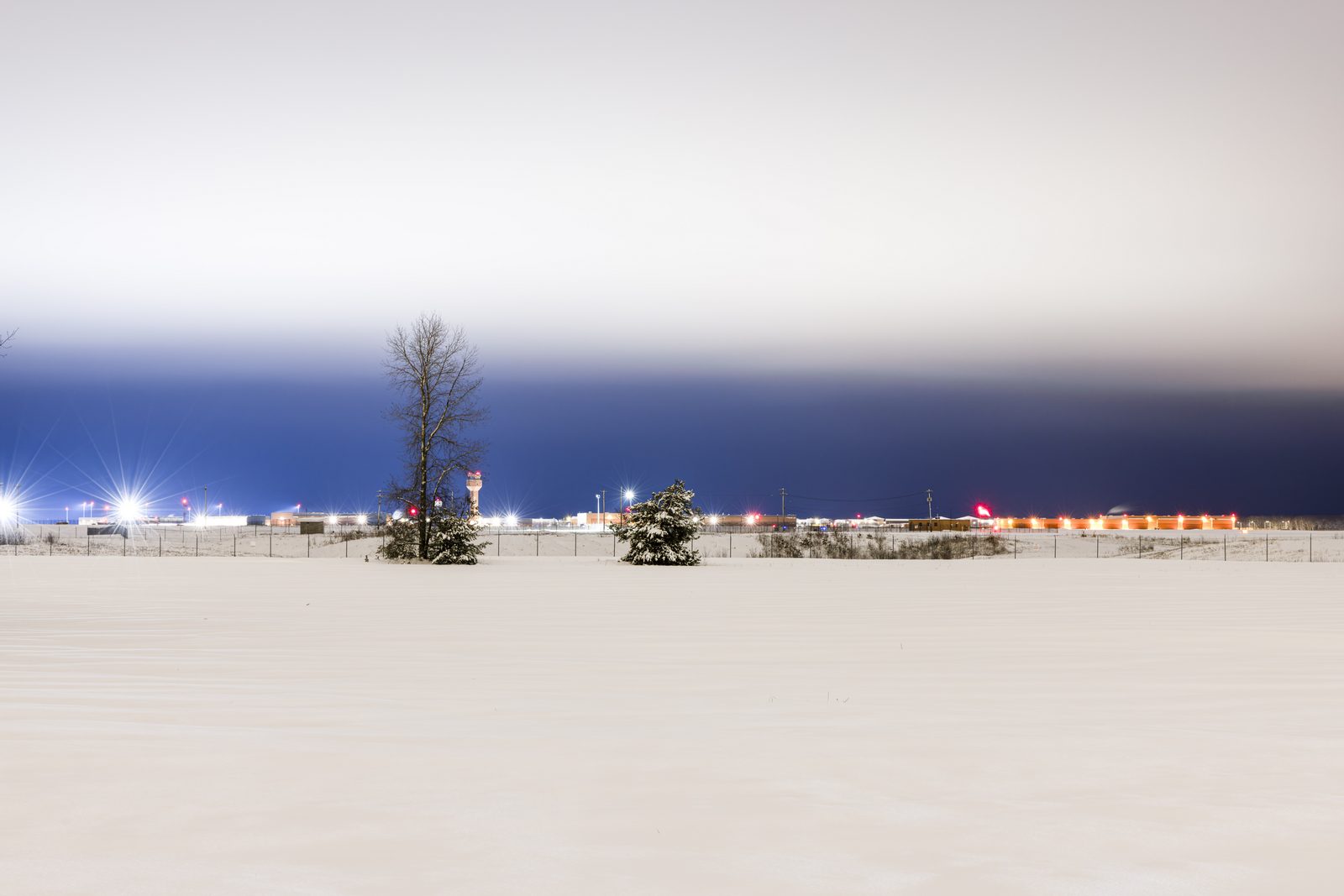 A snow-covered field at blue hour, lights in the distance — Lake Placid