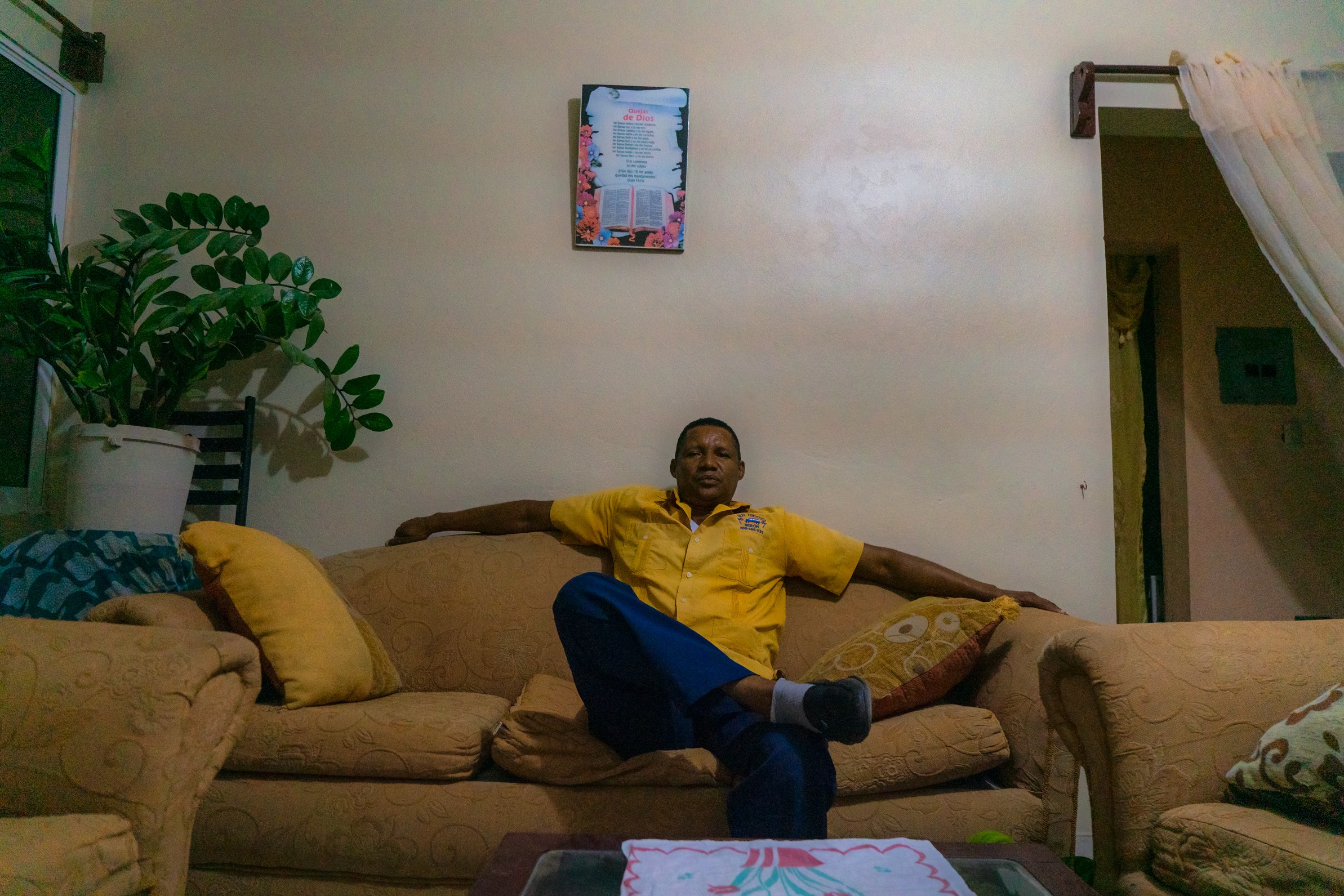 A man in a yellow shirt reclining on a living-room sofa, arms spread along its back — Punta Cana