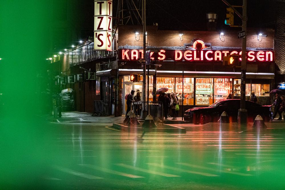 Katz’s Delicatessen in red neon on a rainy night, wet pavement reflecting green light — New York